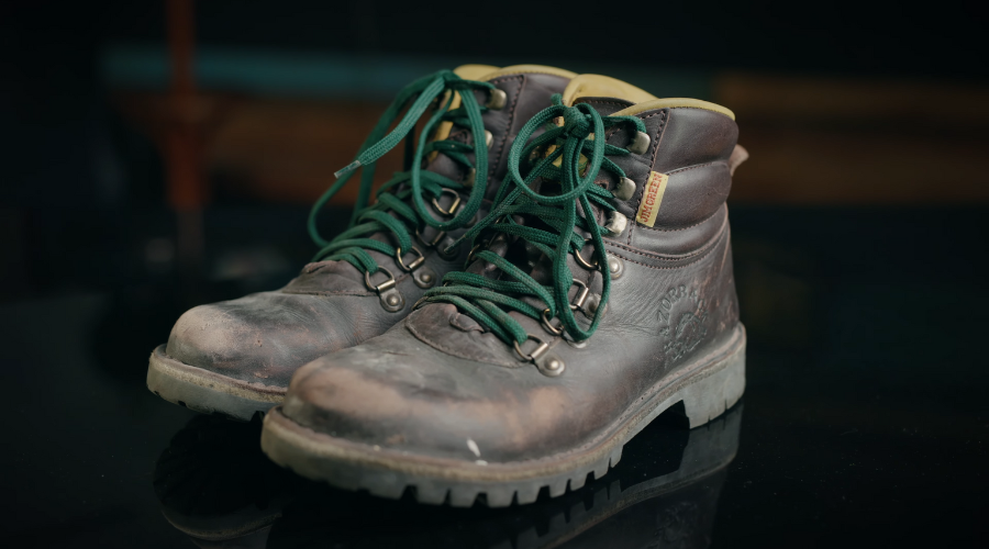 Par iznošenih kožnih radnih čizama sa zelenim pertlama, postavljenih na tamnoj podlozi.