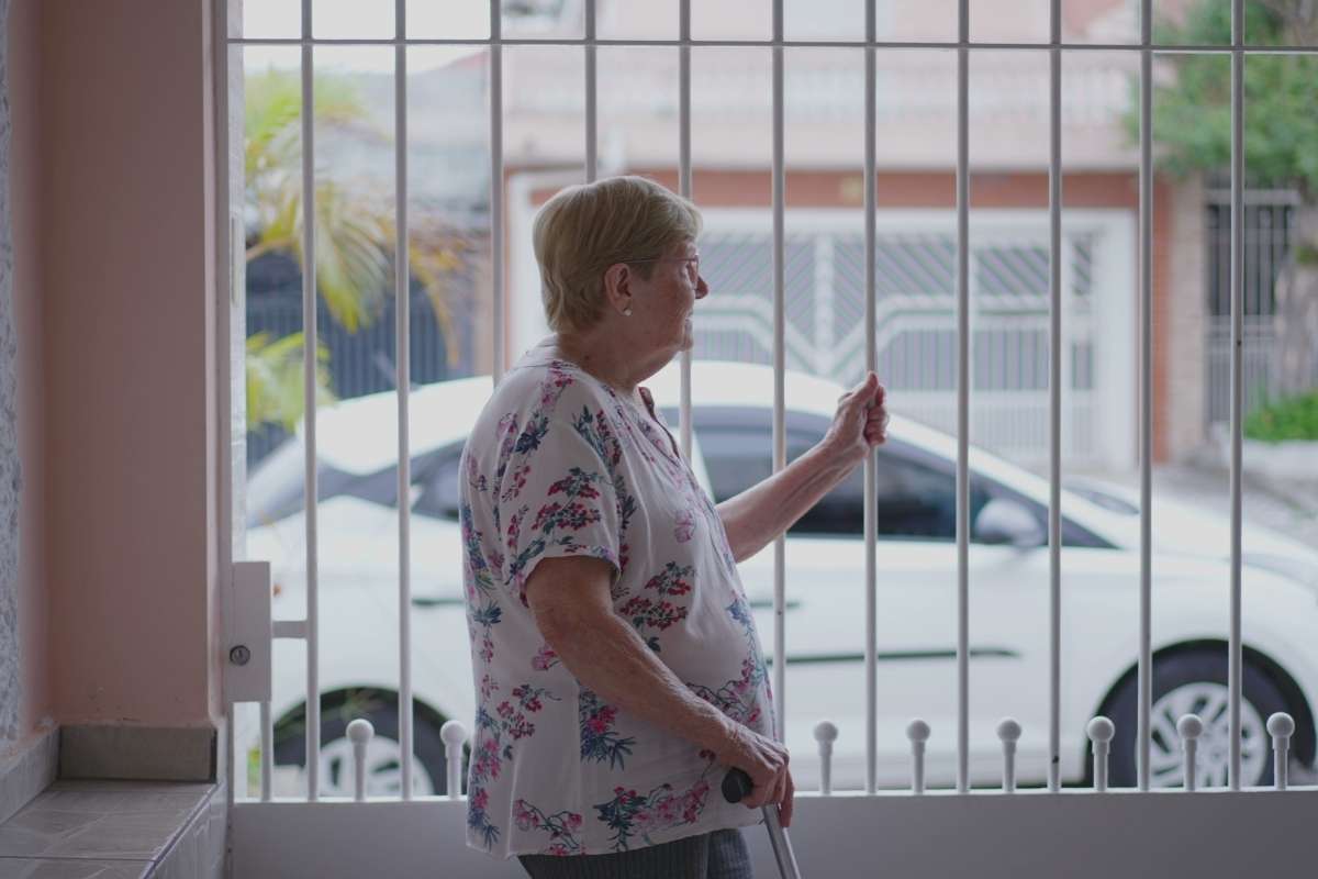 starija žena stoji pored svoje kapije u dvorištu